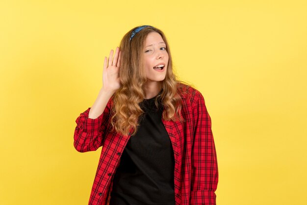 Vista frontale giovane femmina in camicia a scacchi rossa in posa in ascolto su sfondo giallo ragazze emozioni colore modello umano donna