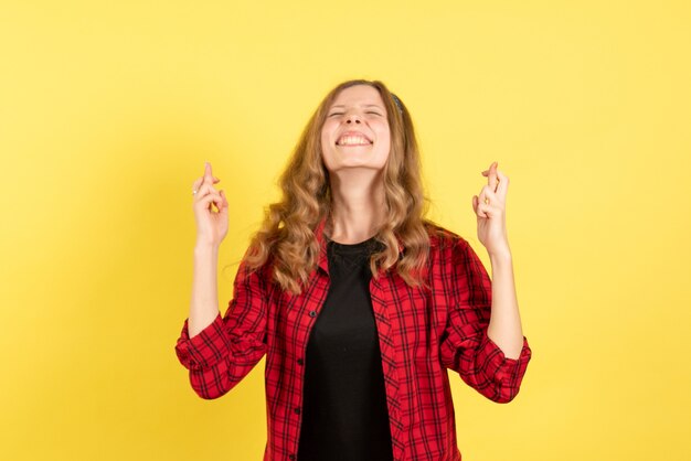 Vista frontale giovane femmina in camicia a scacchi rossa incrociando le dita su sfondo giallo donna emozione umana modello moda ragazza