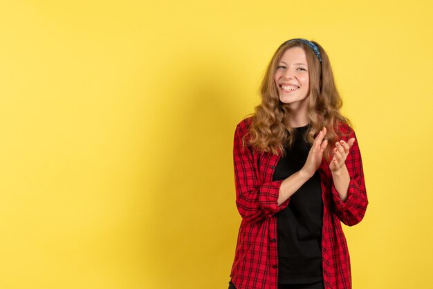 Vista frontale giovane femmina in camicia a scacchi rossa solo in piedi e sorridente su sfondo giallo ragazze modello di colore umano donna