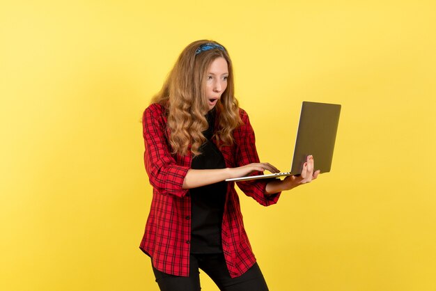 Vista frontale giovane femmina in camicia a scacchi rossa utilizzando il suo computer portatile su sfondo giallo donna emozione umana modello moda ragazza