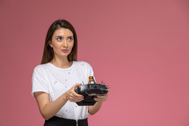 Vista frontale giovane femmina in camicia bianca utilizzando il telecomando sulla parete rosa, modello di posa della donna di colore