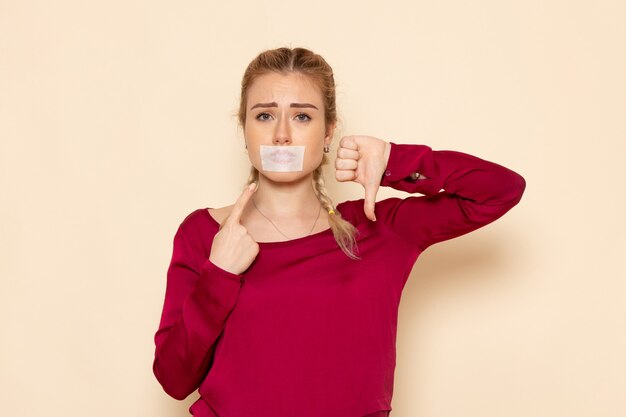 Vista frontale giovane femmina in camicia rossa con la bocca legata che mostra a differenza del segno sullo spazio crema foto panno femminile violenza domestica