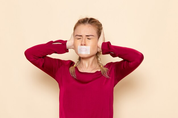 Vista frontale giovane femmina in camicia rossa con la bocca legata orecchie infilzate sullo spazio crema femmina panno foto violenza domestica