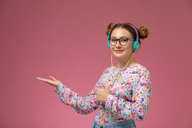 Vista frontale giovane femmina in fiore progettato camicia e blue jeans ascoltando musica con il sorriso sul suo viso su sfondo rosa