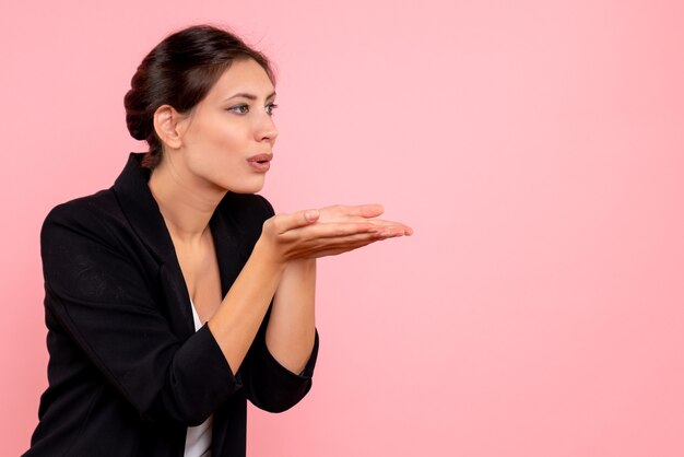 Vista frontale giovane femmina in giacca scura l'invio di baci d'aria su sfondo rosa