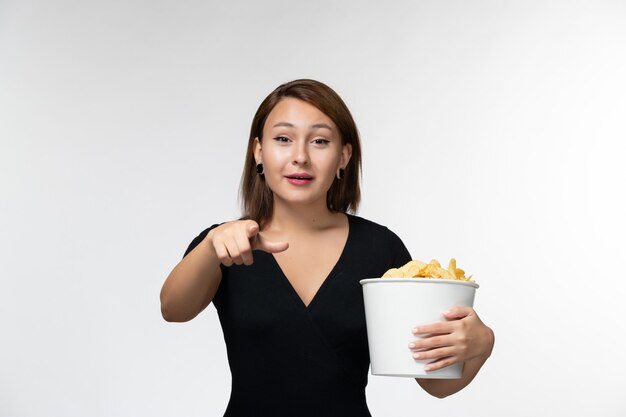 Vista frontale giovane femmina in possesso di patatine fritte e guardare film su superficie bianca