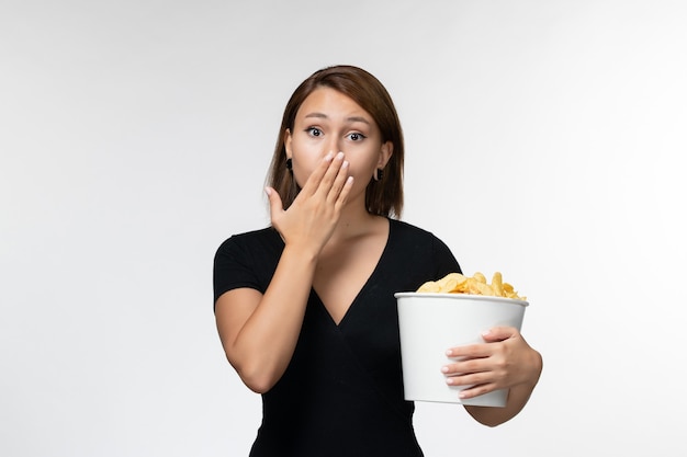 Vista frontale giovane femmina in possesso di patatine fritte e guardare film su superficie bianca