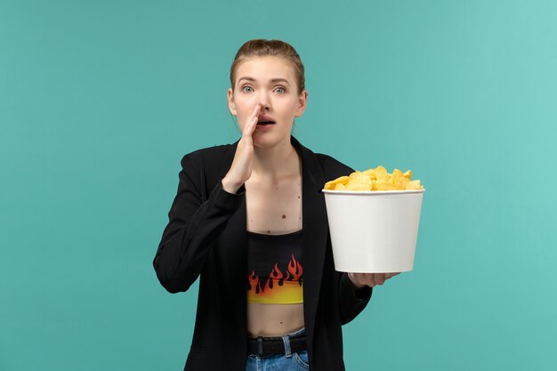 Vista frontale giovane femmina in possesso di patatine fritte e guardare film sulla superficie azzurra