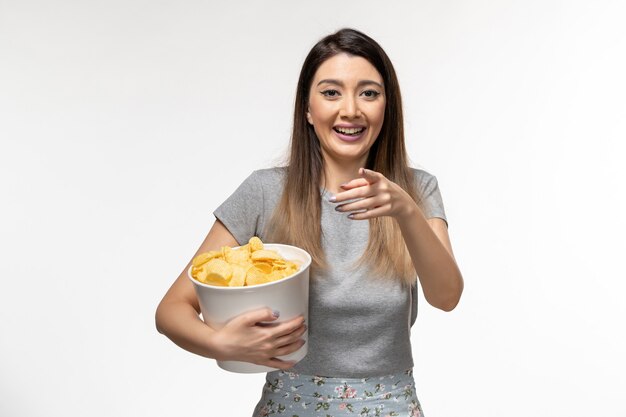 Vista frontale giovane femmina in possesso di patatine fritte mentre si guarda il film che ride sulla superficie bianca