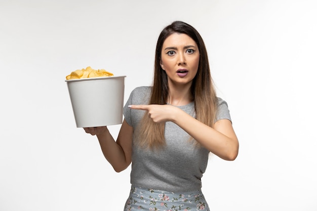 Vista frontale giovane femmina in possesso di patatine fritte mentre si guarda il film sulla superficie bianca