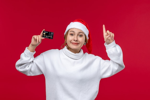 Vista frontale giovane femmina sorridente azienda carta di credito su sfondo rosso