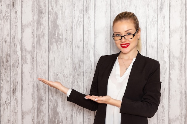 Vista frontale giovane imprenditrice in abiti rigorosi giacca nera con occhiali da sole ottici sorridente sul muro bianco lavoro lavoro ufficio riunioni di affari femminili