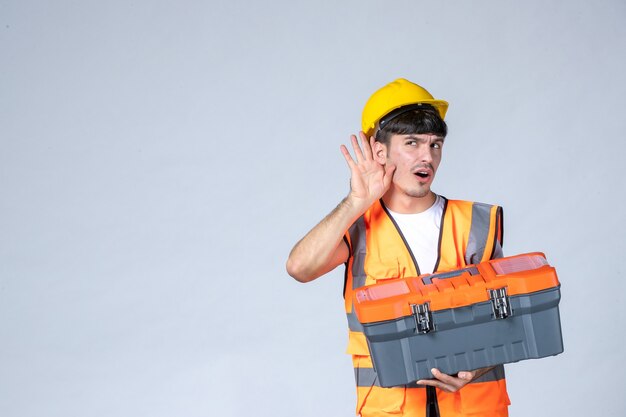 vista frontale giovane lavoratore di sesso maschile in possesso di valigetta portautensili pesante su sfondo bianco