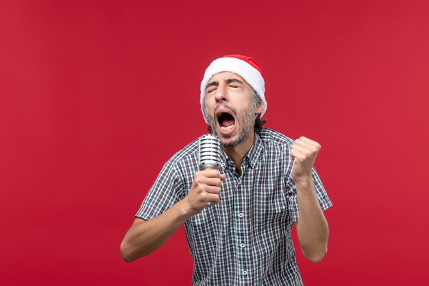 Vista frontale giovane maschio cantando con microfono su sfondo rosso