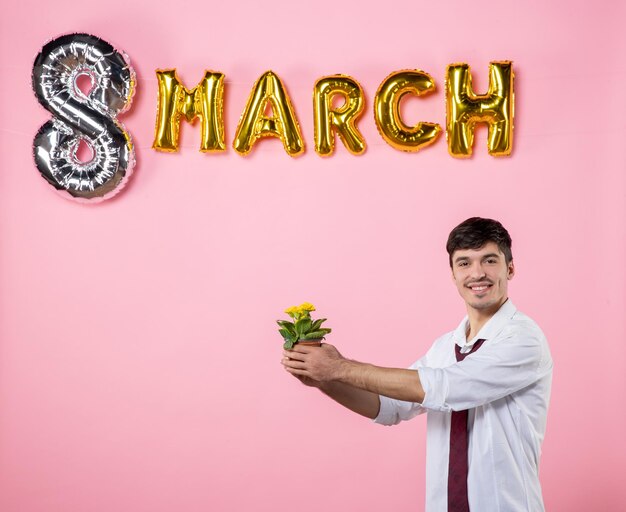 Vista frontale giovane maschio che dà a qualcuno un piccolo fiore come presente di marzo su sfondo rosa uguaglianza colore festa della donna matrimonio festa femminile uomo