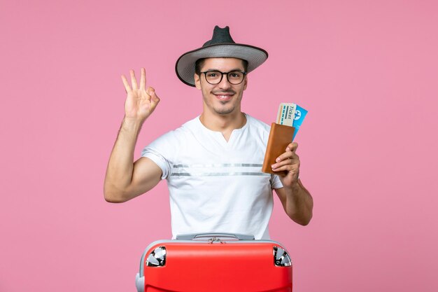 Vista frontale giovane maschio che indossa un cappello e tiene in mano i biglietti dell'aereo sul muro rosa viaggio viaggio aereo foto maschio vacanza a colori