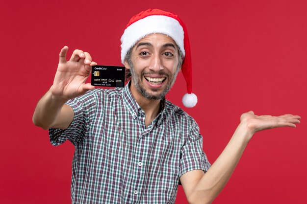 Vista frontale giovane maschio che mostra la carta di credito su sfondo rosso