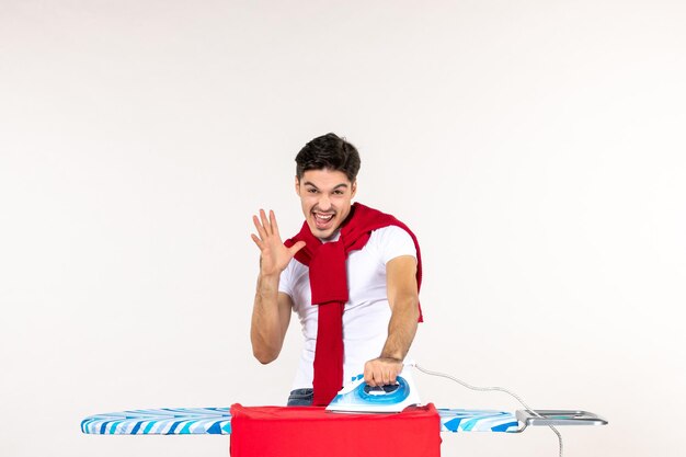 Vista frontale giovane maschio che stira asciugamano rosso su sfondo bianco uomo lavori domestici emozione casa pulito lavoro lavanderia colore