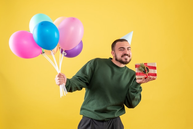 Vista frontale giovane maschio che tiene palloncini colorati e presenti su sfondo giallo