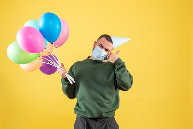 Vista frontale giovane maschio che tiene palloncini colorati su sfondo giallo