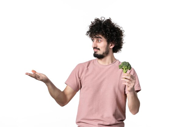 Vista frontale giovane maschio che tiene piccoli broccoli verdi su sfondo bianco corpo vegetale orizzontale dieta umana salute insalata peso
