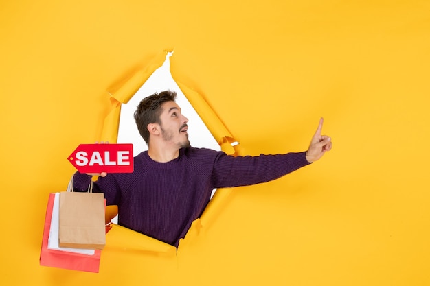 Vista frontale giovane maschio che tiene piccoli pacchetti e vendita scrivendo su sfondo giallo regalo colore vacanza foto shopping