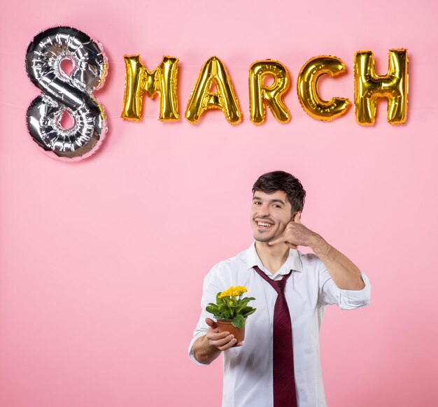 Vista frontale giovane maschio che tiene piccolo fiore in vaso con decorazione di marzo su sfondo rosa colore presente uomo matrimonio uguaglianza festa della donna femminile