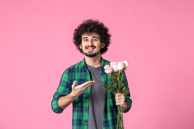 Vista frontale giovane maschio che tiene rose rosa su colore rosa