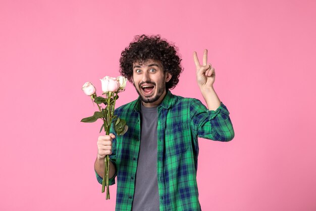 Vista frontale giovane maschio che tiene rose rosa su colore rosa