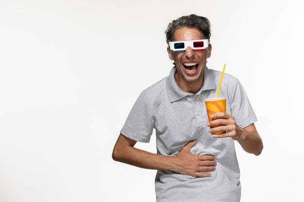 Vista frontale giovane maschio che tiene soda in occhiali da sole d sul godimento di film a distanza muro bianco chiaro solitario