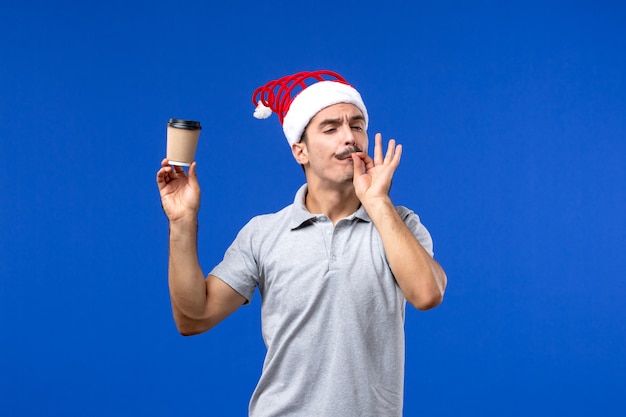 Vista frontale giovane maschio che tiene tazza di caffè di plastica sulla parete blu vacanze di capodanno maschio