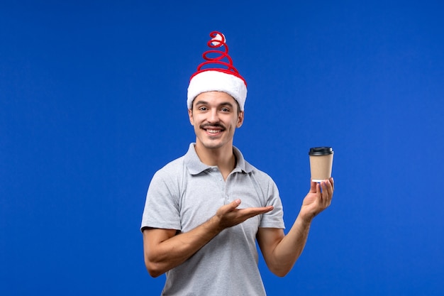 Vista frontale giovane maschio che tiene tazza di caffè sulla parete blu nuovo anno maschio vacanza