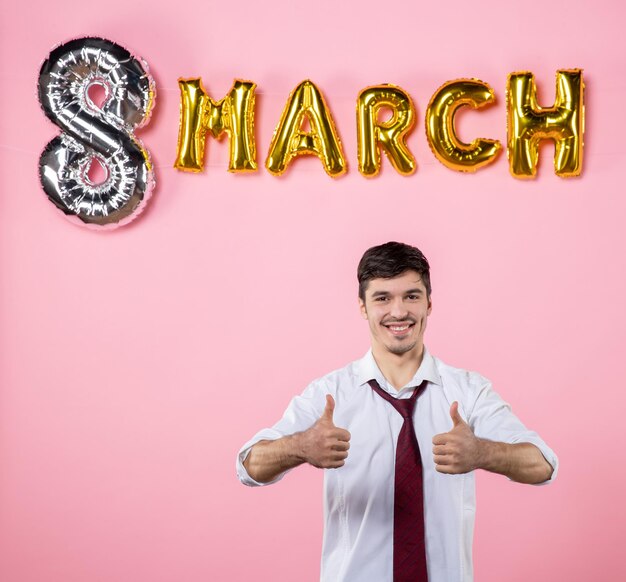 Vista frontale giovane maschio con decorazione di marzo su sfondo rosa colore presente festa di uguaglianza femminile festa della donna uomo