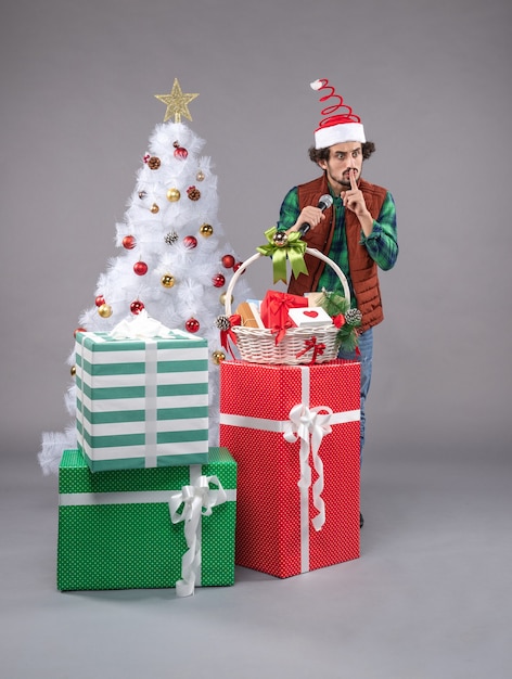 Vista frontale giovane maschio con microfono intorno a regali su grigio