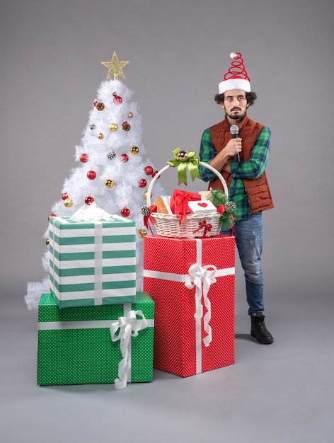 Vista frontale giovane maschio con microfono intorno ai regali sul pavimento grigio regalo di capodanno natale