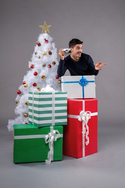 Vista frontale giovane maschio con regali e macchina fotografica sulla scrivania grigia vacanza capodanno natale