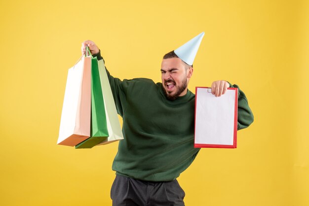 Vista frontale giovane maschio holding shopping packages e nota su sfondo giallo