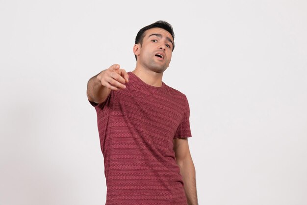 Vista frontale giovane maschio in maglietta rosso scuro in piedi e sottolineando su sfondo bianco