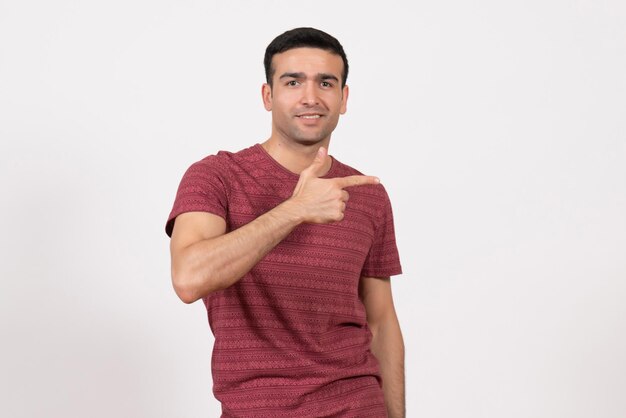 Vista frontale giovane maschio in maglietta rosso scuro in posa su sfondo bianco chiaro