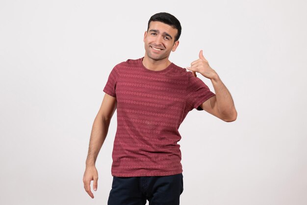 Vista frontale giovane maschio in maglietta rosso scuro sorridente e in piedi su sfondo bianco