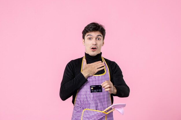 Vista frontale giovane maschio in mantello con carta di credito nera su sfondo rosa lavoro lavoratore colore professione cucina uniforme capo cucina orizzontale