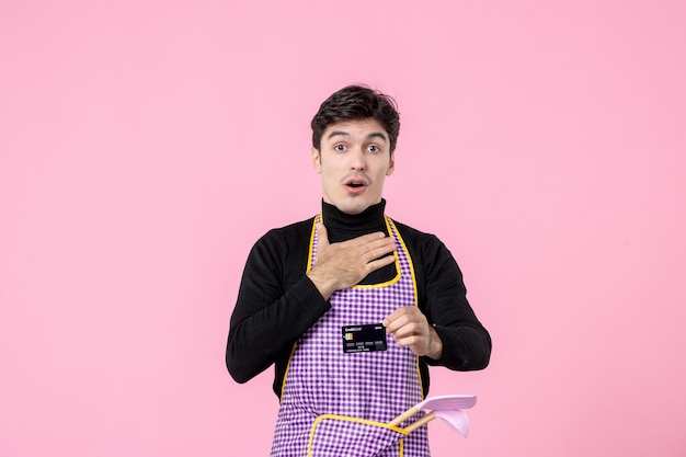 Vista frontale giovane maschio in mantello con carta di credito nera su sfondo rosa lavoro lavoratore colore professione cucina uniforme capo cucina orizzontale