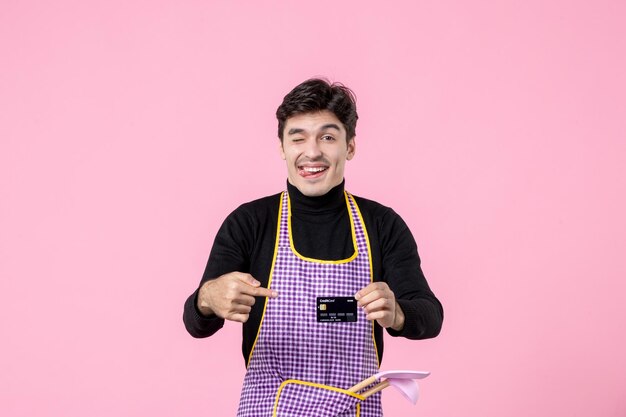 Vista frontale giovane maschio in mantello con carta di credito nera su sfondo rosa lavoro lavoratore colore professione uniforme denaro capo cucina orizzontale