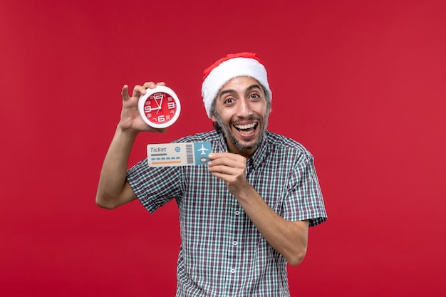 Vista frontale giovane maschio in possesso di biglietto con orologio su sfondo rosso