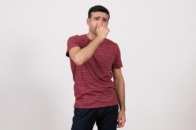 Vista frontale giovane maschio in t-shirt in posa chiudendo il naso su sfondo bianco