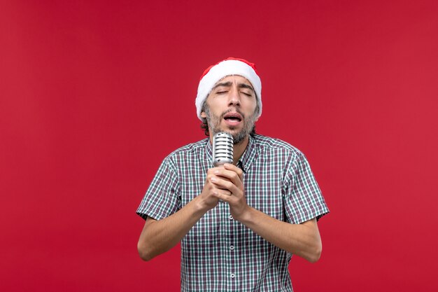 Vista frontale giovane maschio tenendo il microfono e cantando su sfondo rosso