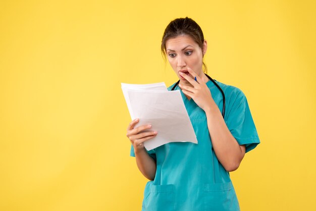 Vista frontale giovane medico femminile in camicia medica con documenti su sfondo giallo