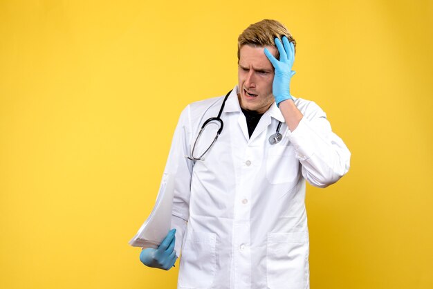 Vista frontale giovane medico maschio che tiene analisi sul virus umano giallo scrivania salute medic