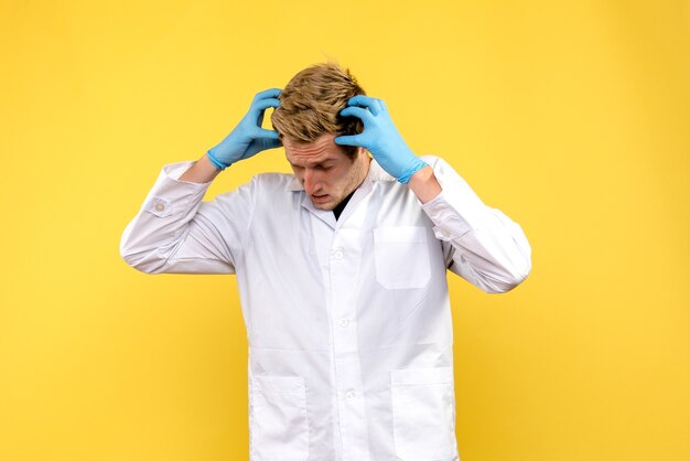 Vista frontale giovane medico maschio esitando su sfondo giallo medico pandemico covid umano