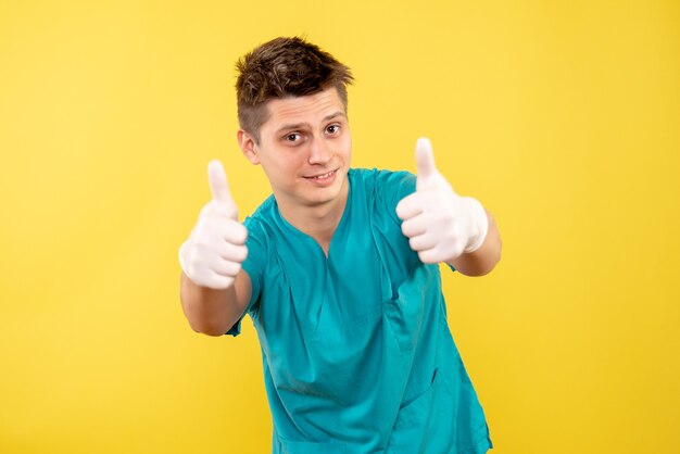 Vista frontale giovane medico maschio in tuta medica con guanti su sfondo giallo
